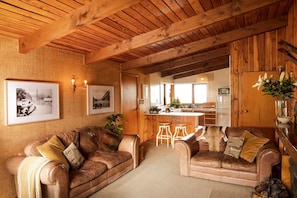 Ein gemütliches Wohnzimmer mit Holzboden, zwei Ledersofas, einer Küchenzeile und gerahmten Bildern an der Wand.