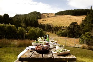 A picnic table with food and drinks in a natural setting with hills and trees in the background.