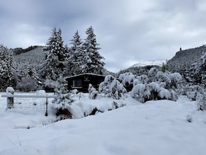 A snow-covered landscape with a building that appears to be a lodge or cabin, surrounded by trees and a fence.