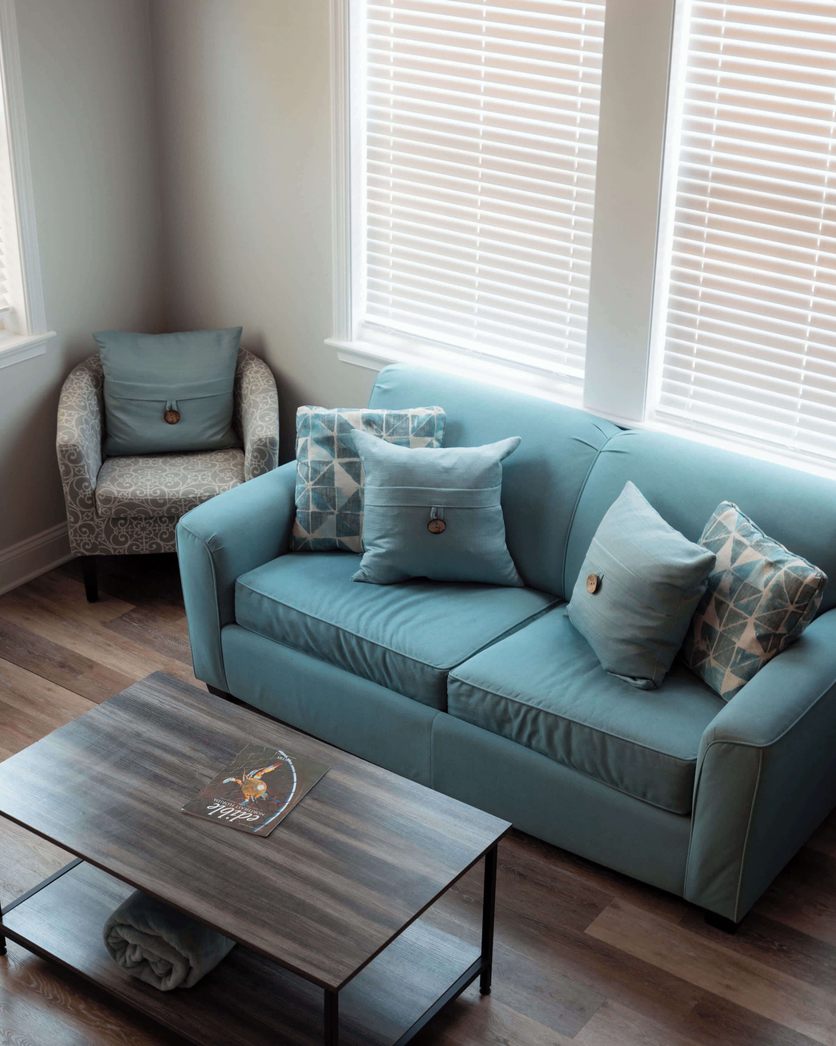 A living room with a teal sofa, patterned armchair, and a coffee table with a map design.