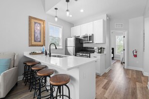 A modern kitchen with white cabinets, stainless steel appliances, and a central island with stools. - Villa Mojito Apartment A in Historic Downtown (St. Augustine)