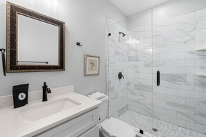 A bathroom with a white sink, a mirror, a framed picture, and a shower with white tiles. - Villa Mojito Apartment A in Historic Downtown (St. Augustine)