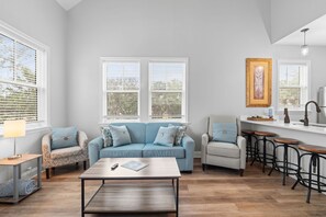 A living room with a sofa, armchairs, a coffee table, and a kitchen area with stools. - Villa Mojito Apartment A in Historic Downtown (St. Augustine)