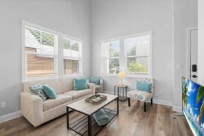 A living room with a sofa, coffee table, armchair, TV, and windows with blinds. - Villa Mojito A&B | Historic Downtown (St. Augustine)