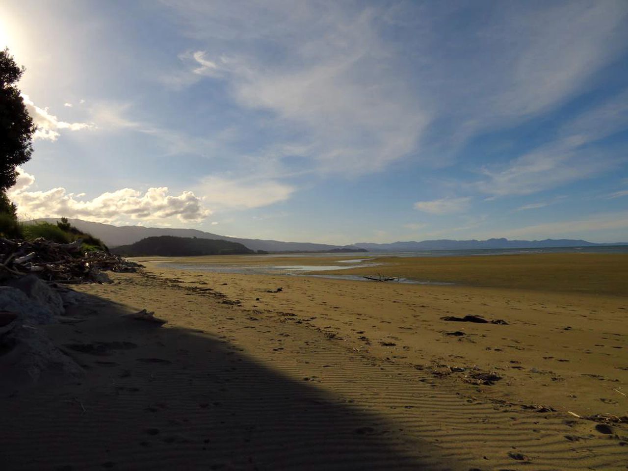 Una playa con cielo despejado, montañas lejanas y mar tranquilo.