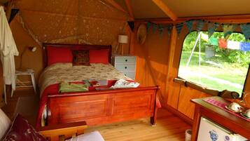 A tent-style bedroom with a wooden bed, a small desk, and a window with a view of greenery.