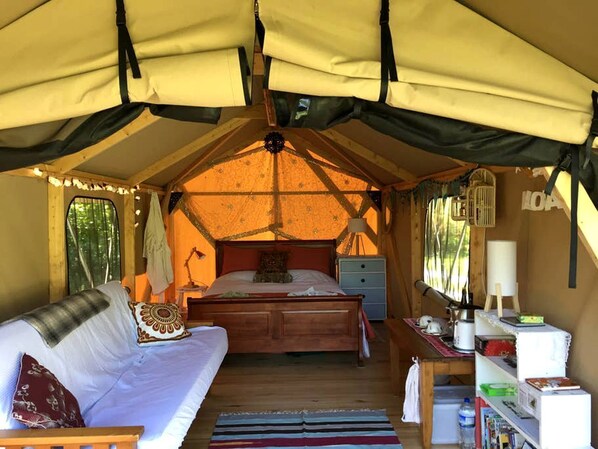 A tented accommodation with a bed, a sofa, a bedside table, and a small cabinet.
