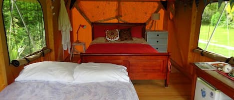 Een knus kamertje in tentstijl met een bed, een klein bureau en een koelkast.