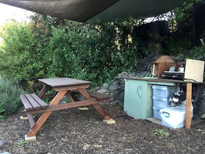 A picnic table and a small outdoor kitchen area with a stone wall and greenery in the background. - Glamping Tent on Permaculture Farm near Pohara Beach in Golden Bay, South Island (Pohara)