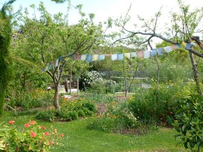 A garden with various plants and flowers, a tree with a colorful banner, and a greenhouse structure in the background.