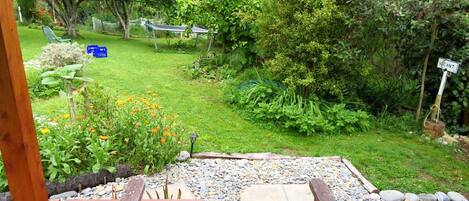 A wooden deck with a table and chairs, surrounded by a garden with various plants and a small pond.