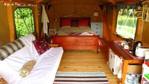 L’intérieur d’un chalet accueillant, avec un lit, une petite kitchenette et une fenêtre donnant sur un paysage verdoyant.