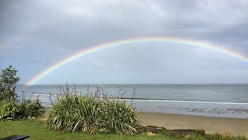 Une plage avec un arc-en-ciel, de l’herbe et deux tables de pique-nique.