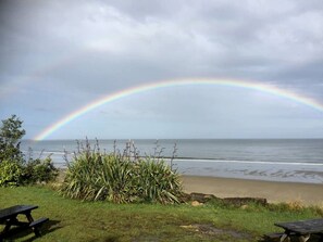 A beach with a rainbow, grass, and two picnic tables.