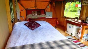 A cozy room with a bed, a small desk, a chair, and a window with a view of greenery.