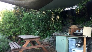 Une table de pique-nique et un petit espace cuisine extérieur, avec un mur en pierre et de la verdure en arrière-plan.