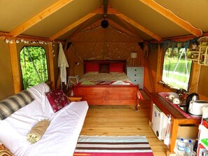 Interior acogedor de una cabaña con una cama, un pequeño rincón de cocina y una ventana con vistas a la vegetación.