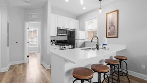 A modern kitchen with white cabinetry, stainless steel appliances, and a central island with stools. - Villa Mojito Unit B in Historic Downtown (St. Augustine)