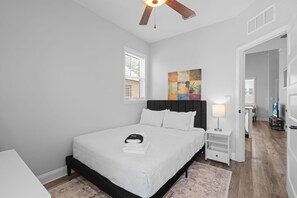 A bedroom with a bed, bedside tables, a ceiling fan, a painting, and a television in the background. - Villa Mojito Unit B in Historic Downtown (St. Augustine)