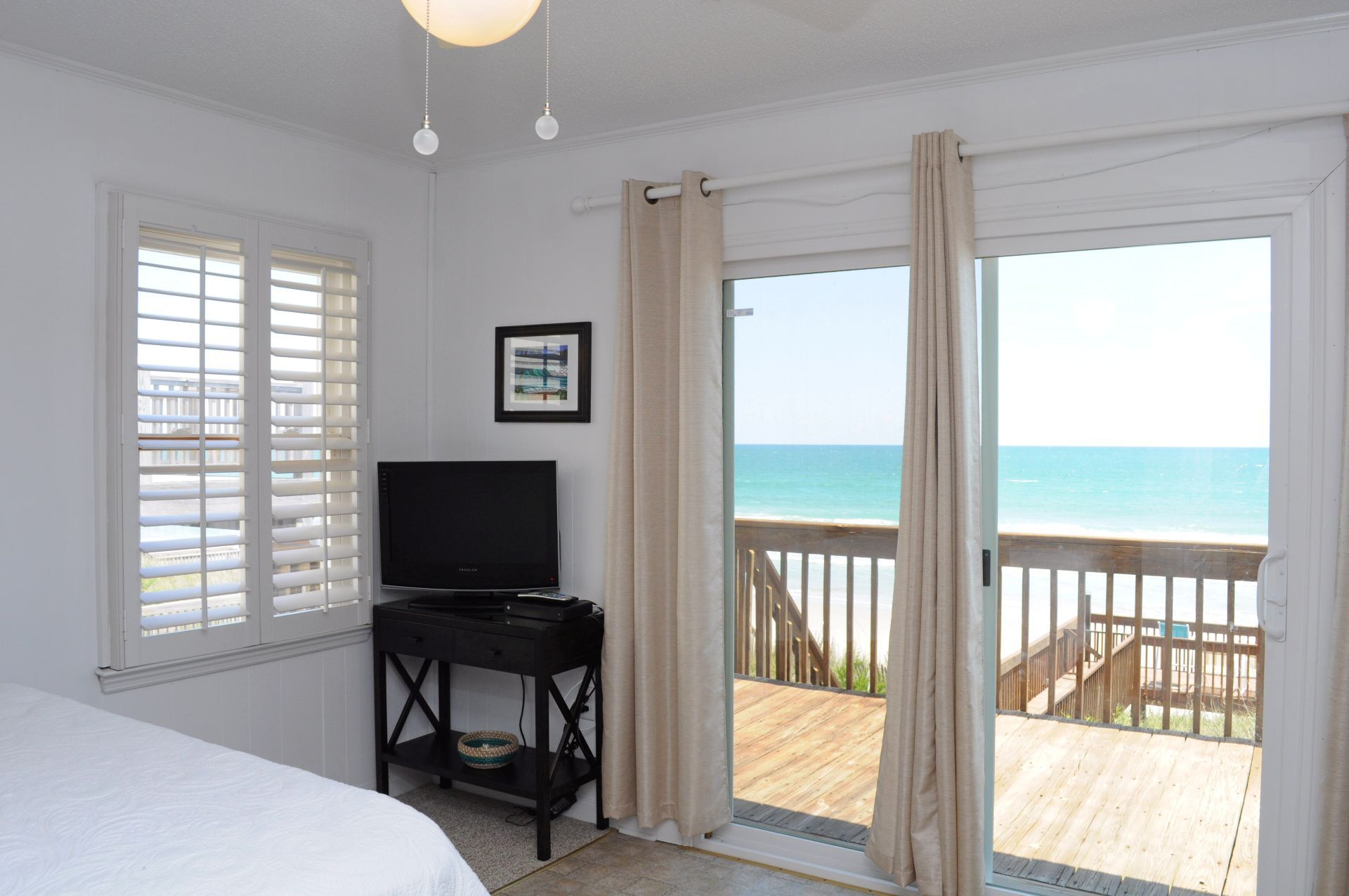 A bedroom with a bed, a television, and a view of the ocean through a sliding glass door.