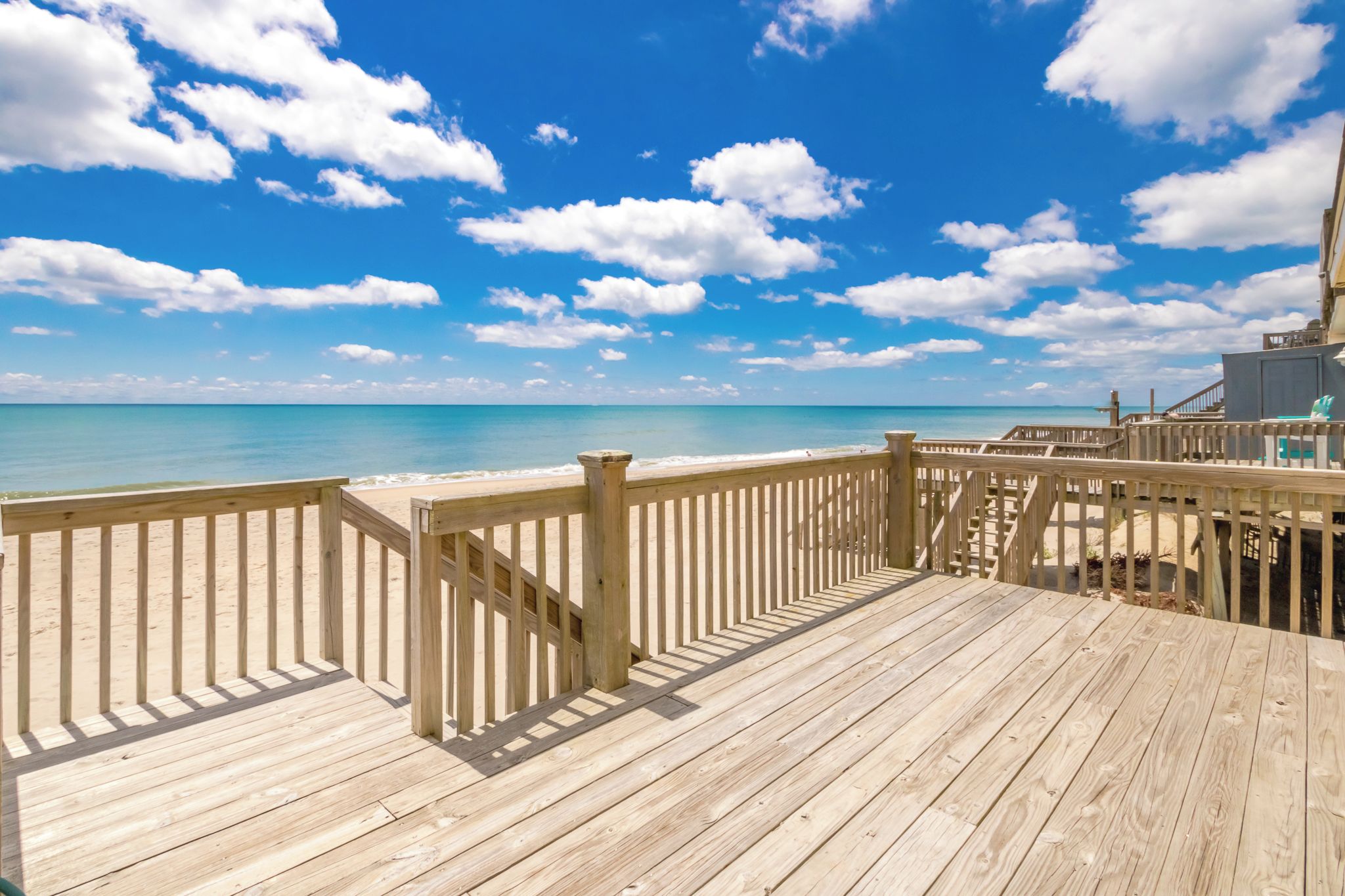 A wooden deck with a railing overlooking a beach and ocean.