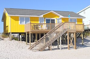 A two-story yellow building with a wooden deck and stairs leading to a balcony. - Sea-Renity Oceanfront 4 bedroom, 2 bath home in Surf City! (Surf City)