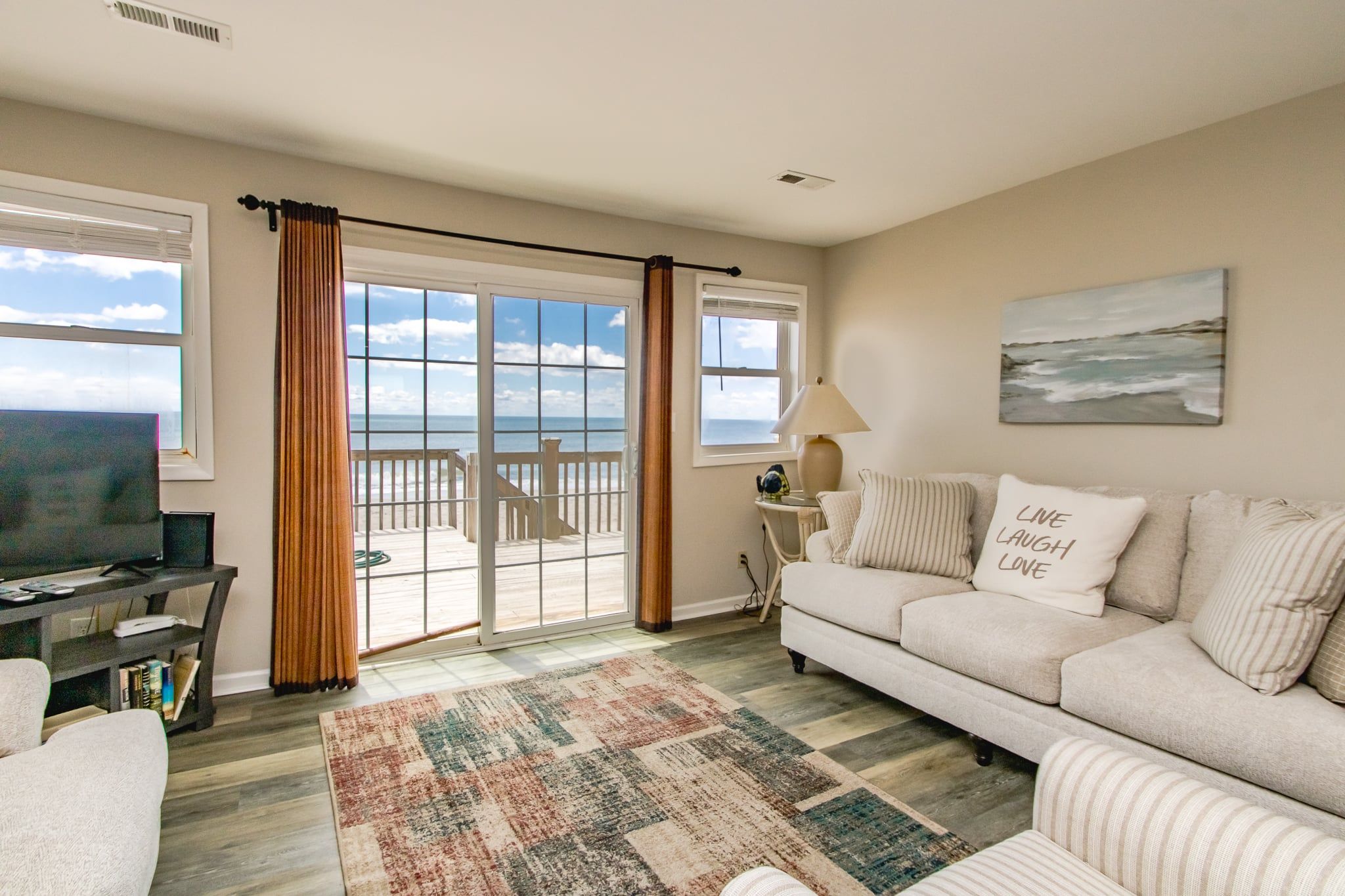 A living room with a sofa, a television, a rug, and a view of the ocean through large windows.