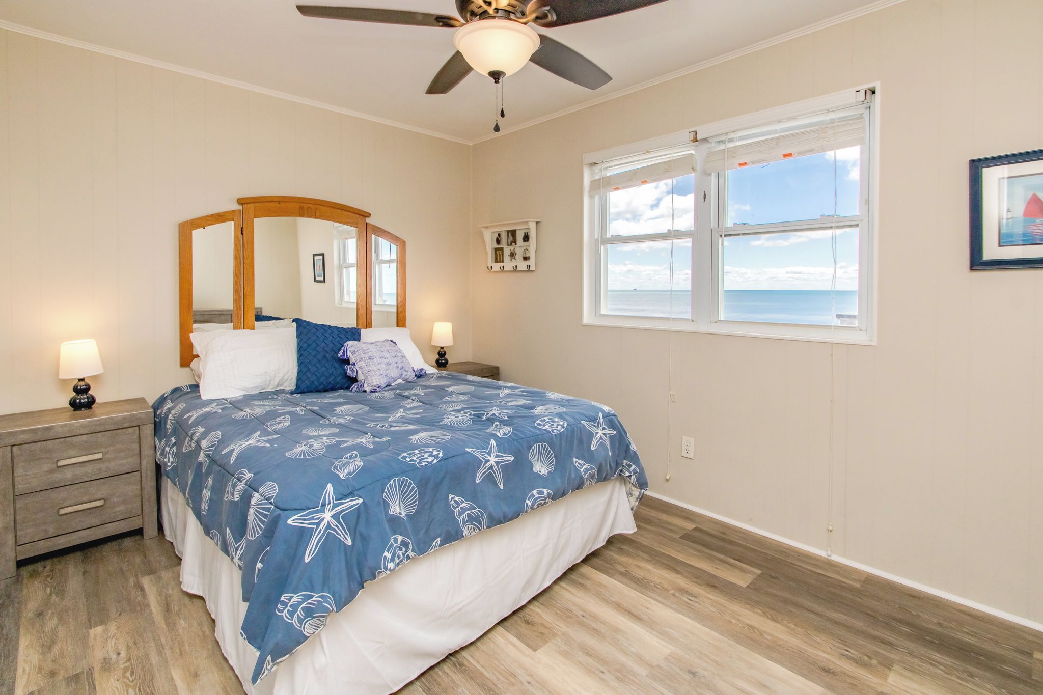 A bedroom with a bed, nightstands, a ceiling fan, a window with a view, and a wall-mounted shelf.