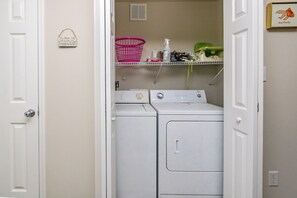 Une buanderie équipée d’un lave-linge et d’un sèche-linge, avec un panier rose et une étagère contenant des produits de nettoyage.