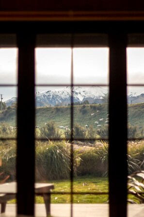 A view through a window with a mountain landscape, including snow-capped peaks and a flock of sheep.