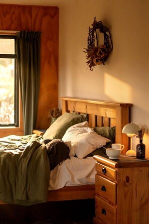 Un dormitorio con cabecera de madera, una mesita de noche con lámpara y una ventana con cortinas.