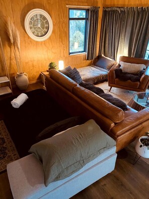 Una habitación acogedora con un sofá de cuero marrón, un sillón blanco, una mesita redonda y un reloj de pared grande.