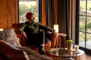 A person seated on a leather sofa in a room with a view of greenery outside.