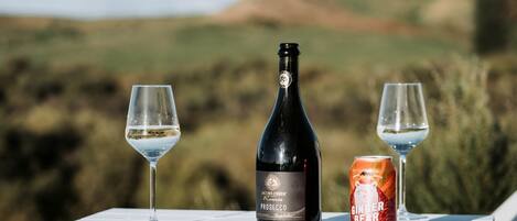 A bottle of Jacob's Creek Prosecco, two glasses of wine, and a can of Ginger Bear on a white table with a scenic outdoor view.