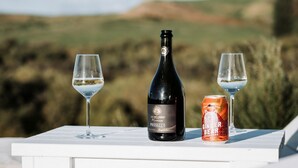 A bottle of Jacob's Creek Prosecco, two glasses of wine, and a can of Ginger Bear on a white table with a scenic outdoor view.