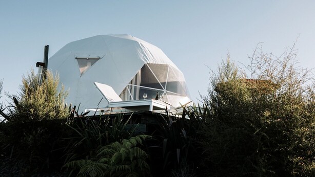 A geodesic dome structure with a table and chairs in front, surrounded by vegetation.