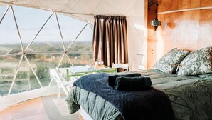 A room with a bed, a table, and a view through a large window.