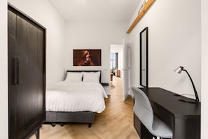 Une chambre à coucher avec un lit, un bureau, une chaise, une armoire et un tableau accroché au mur.