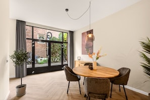 Un coin repas comprenant une table ronde en bois, quatre chaises, un luminaire suspendu et une plante en pot.