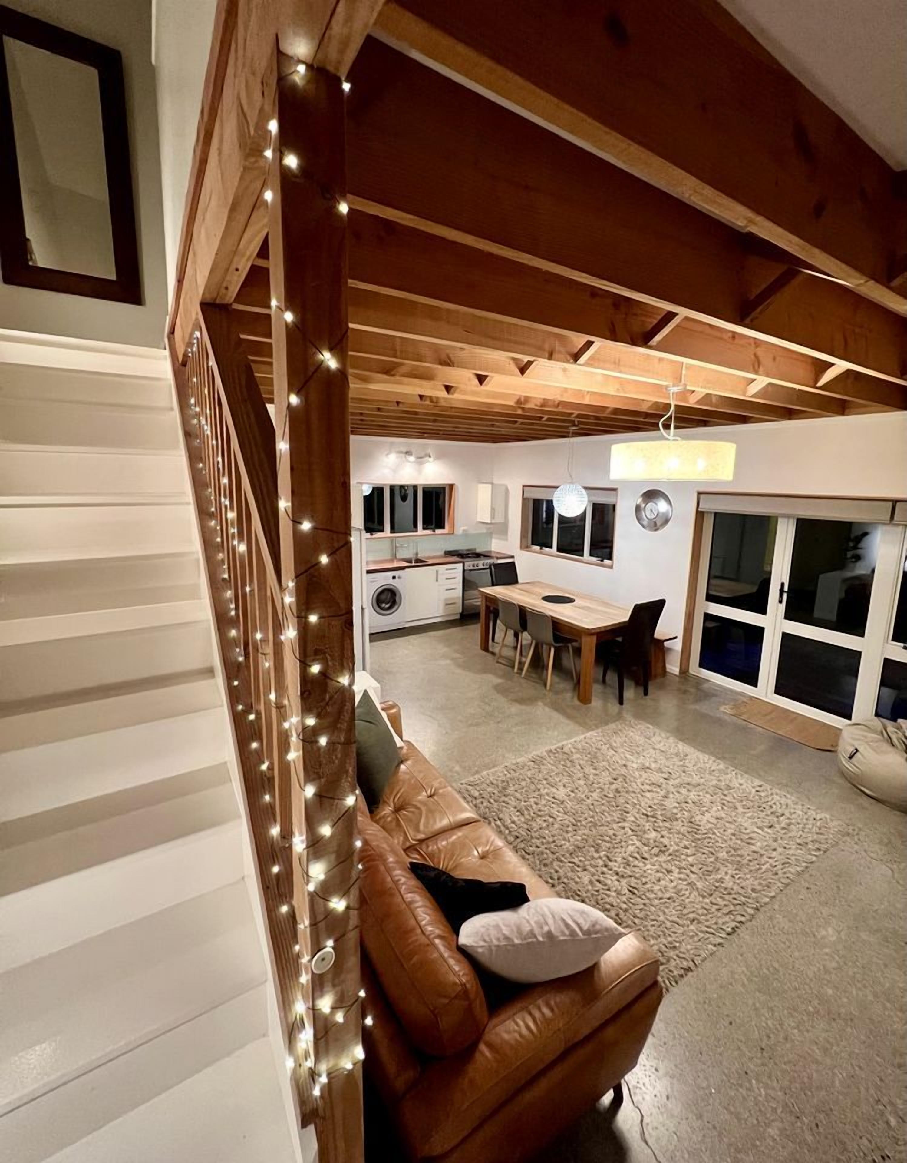 A spacious living area with a wooden ceiling, a brown leather sofa, a dining table, and a kitchen in the background.