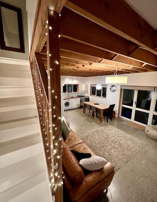 A spacious living area with a wooden ceiling, a brown leather sofa, a dining table, and a kitchen in the background.