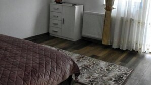 Un dormitorio con cama, cómoda, televisor de pantalla plana, radiador y ventana con cortinas.