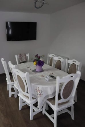 Ein Essbereich mit einem runden Tisch, weißen Stühlen, einer Tischdecke mit Blumenmuster und einer Vase mit Blumen.
