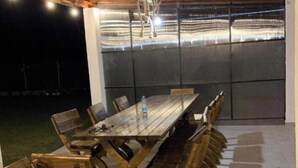 Mesa y bancos de madera al aire libre, una lámpara colgante y vista a un estadio a través de un muro de cristal.
