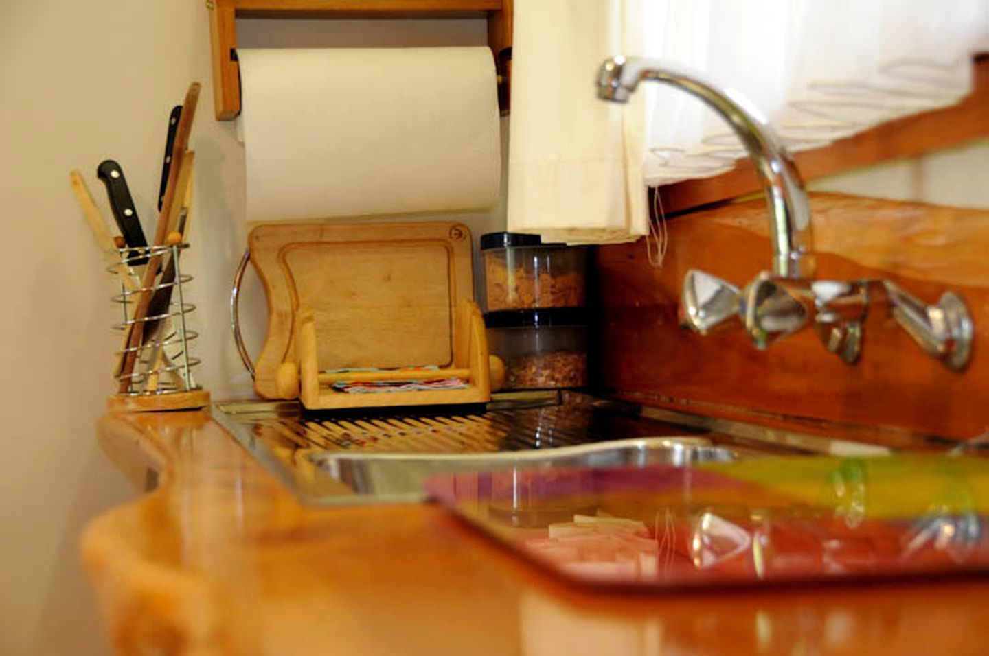 A kitchen with a wooden countertop, a sink, a roll of paper towels, and a spice rack.