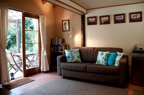 A cozy living room with a brown sofa, floral cushions, a bookshelf, and a coffee machine.