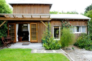 A wooden house with a covered patio, a garden with various plants, and a small outdoor seating area.