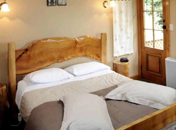 A wooden bed with white bedding, a bedside table with a lamp, and a window with curtains.