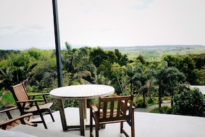 A wooden table and chairs on a balcony with a view of a lush landscape.