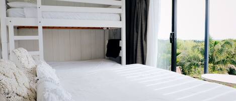 Een slaapkamer met een stapelbed, een groot raam met uitzicht op groen en een klein tafeltje.